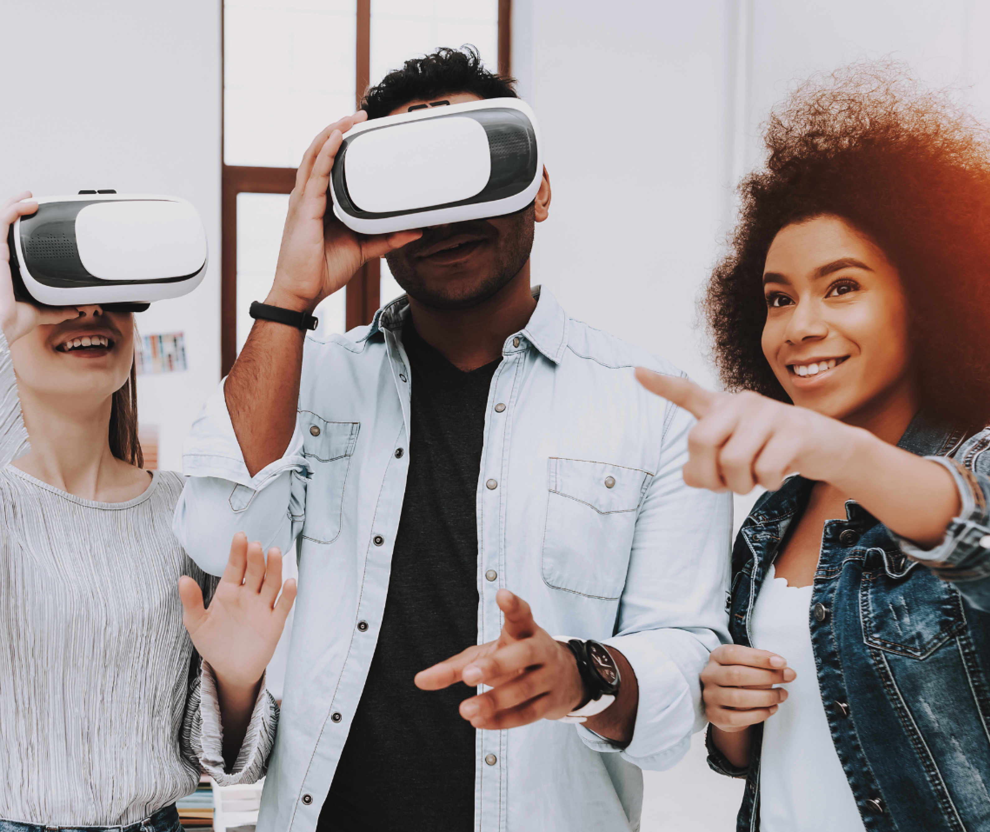 Image of two people wearing Virtual Reality headsets with another person pointing a finger to the distance